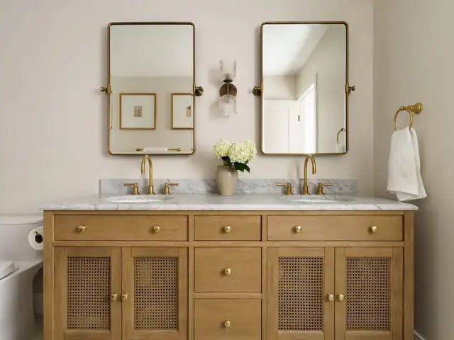 Remodeled San Diego bathroom with oak cane-front double vanity, marble countertop and brass pivot mirrors