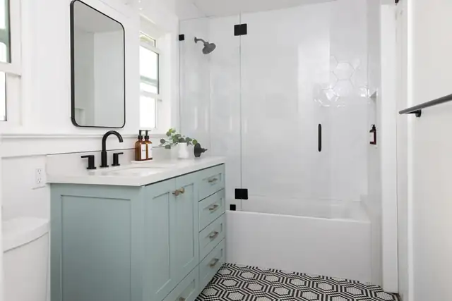 Remodeled bathroom with a sage green vanity, frameless glass shower and geometric mosaic floor tile
