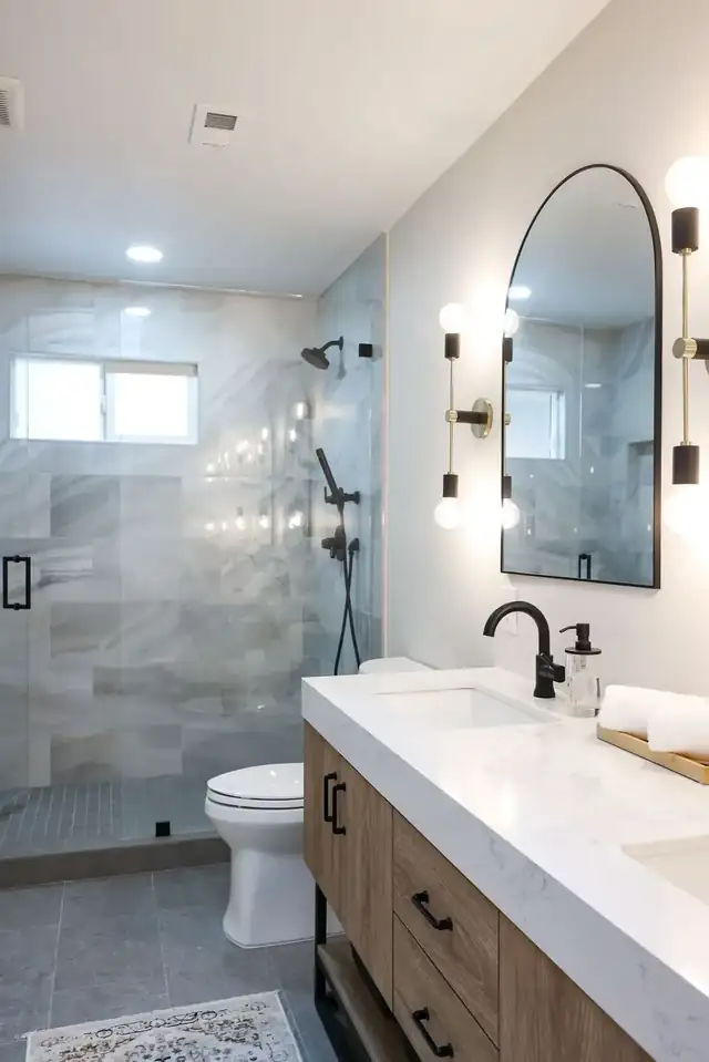 Scripps Ranch bathroom remodel with walk-in glass shower beside a wood vanity and arched mirror